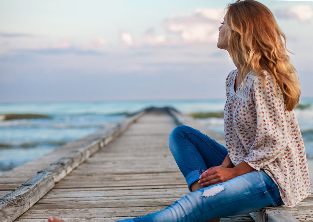 Frau sitzt auf einem Steg am Meer und blickt in die Ferne